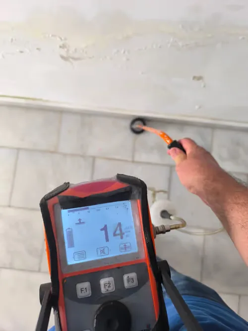 Técnico con detector de fugas junto a una pared con humedad