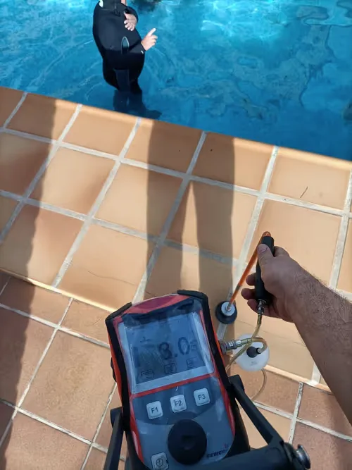 Técnico con detector de fugas junto al borde de una piscina
